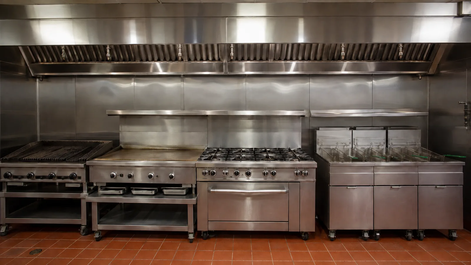 Una línea larga de restaurante americano bajo una sola campana continua: parrilla de carbón, plancha, estufa de seis quemadores y un banco de freidoras.