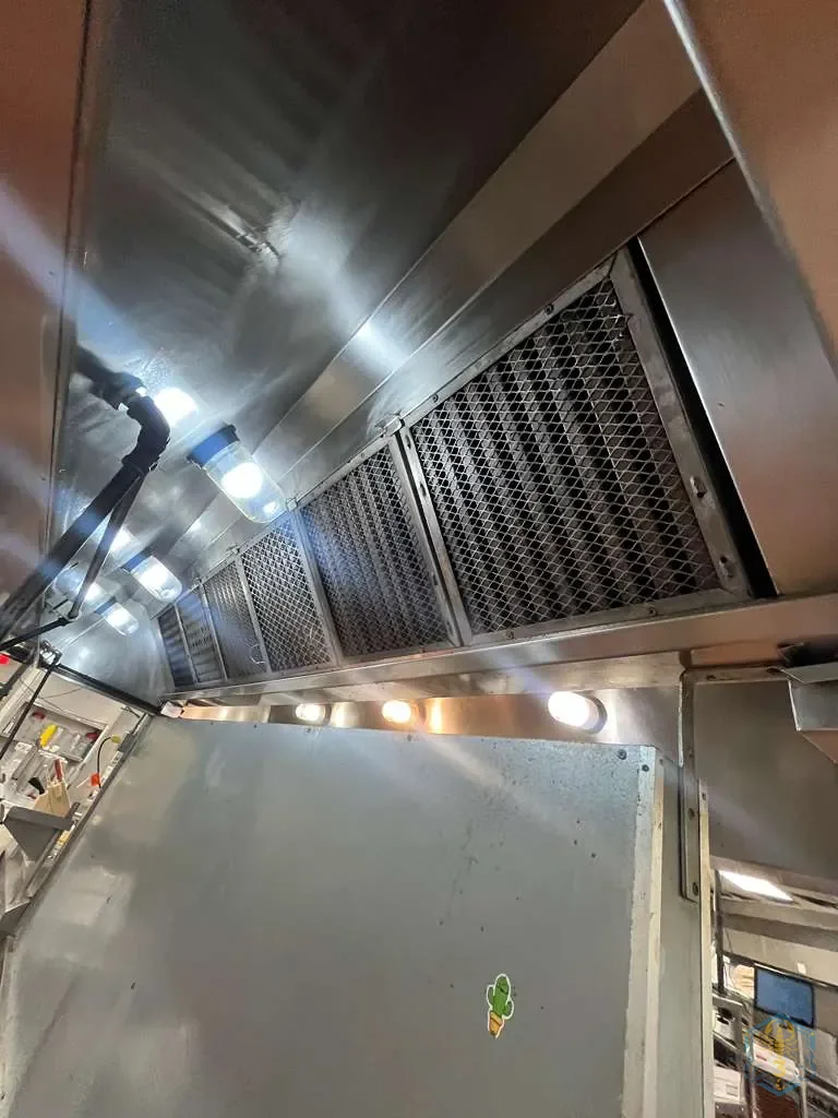 Filtros de malla reinstalados en la campana, vistos desde abajo a lo largo de la línea de cocina.