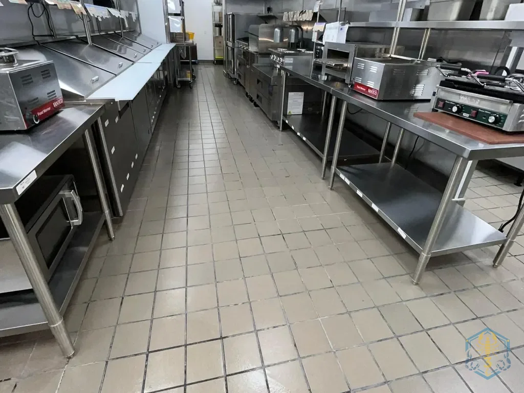 A commercial kitchen after cleaning: stainless tables, shelving and a dry, clean tile floor.