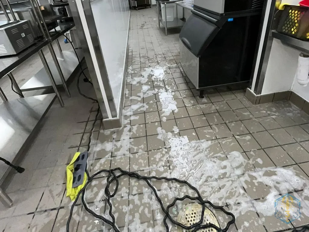 Back-of-house floor mid-wash: degreaser foam running across the tile to the floor drain, hose on the floor.