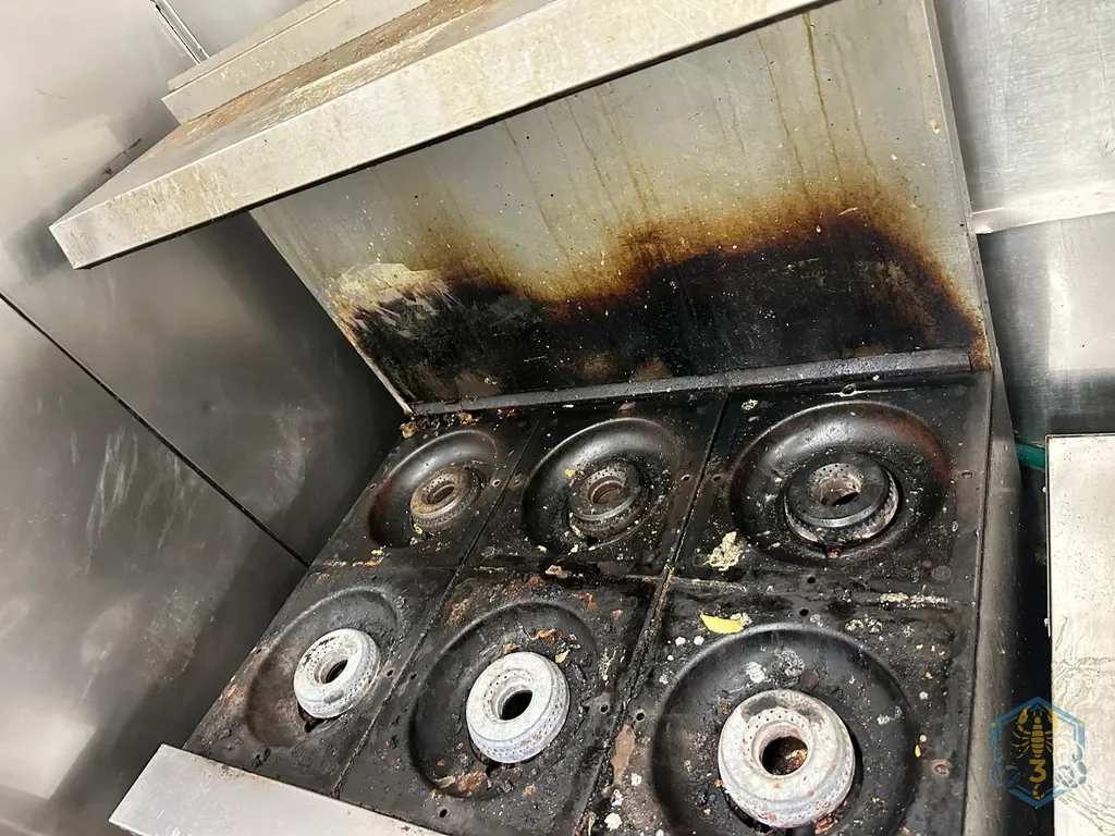 Six-burner range before cleaning: the back splash is black with baked-on grease and the burner heads are crusted.